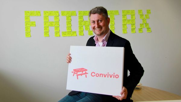 Steve Parks, Convivio CEO, holds the Convivio logo. Behind him on the wall, sticky notes spell out Fair Tax
