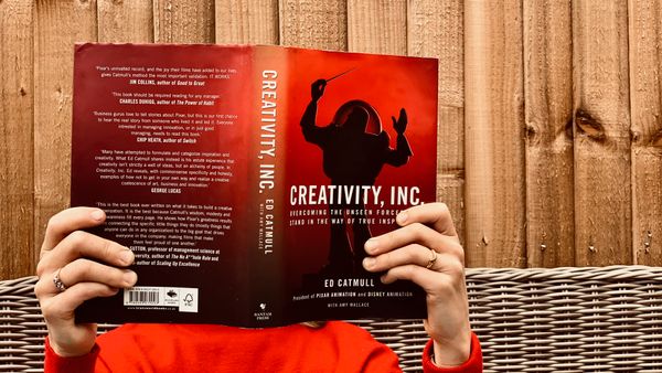 Woman in a red sweater reading Creativity, Inc., by Ed Catmull